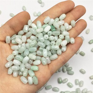 Pode incluir: Um grande monte de contas de jade ovaladas de cor verde claro. As contas são lisas e polidas, e têm um aspeto natural e terroso.