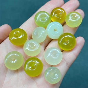 May include: A collection of round, smooth, green and yellow jade beads with a hole in the center. The beads are arranged on a hand.
