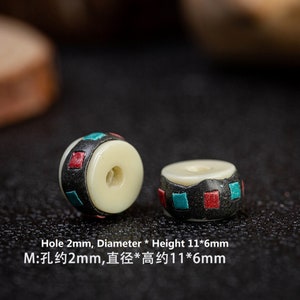 May include: Two white bone beads with black, red, and blue geometric patterns. The beads have a hole in the center and measure approximately 11 mm in diameter and 6 mm in height. The hole is approximately 2 mm in diameter.