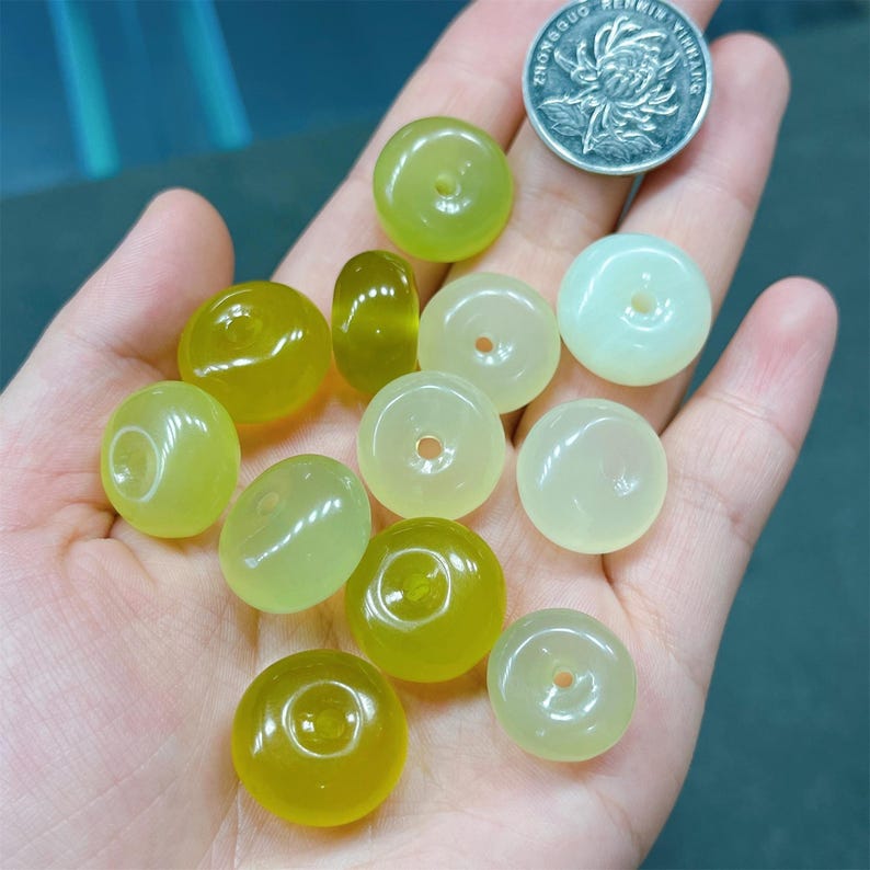 May include: A collection of 12 green jade donut beads. The beads are various shades of green and have a smooth, polished finish.