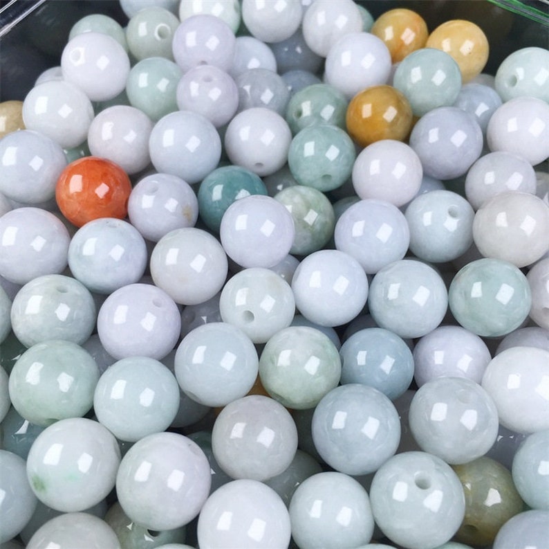May include: A collection of round, smooth, light green jade beads. The beads are various shades of green, white, and light orange.