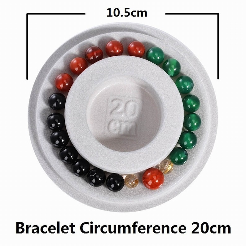 May include: A white circular display with a 20cm circumference measurement for bracelets. The display has a ring of green, red, and black beads around the outer edge.