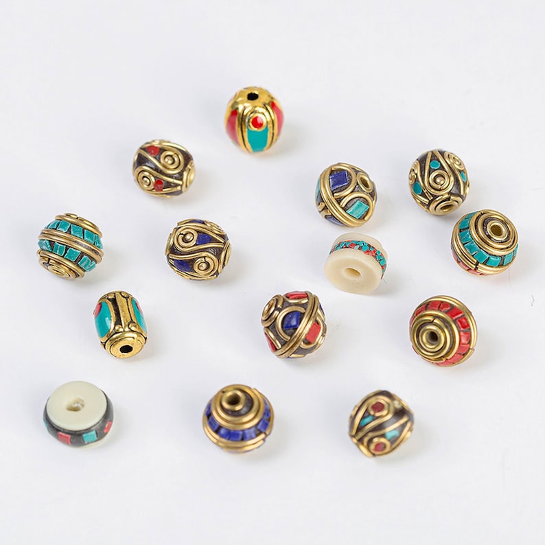 May include: Assortment of round and oval beads with intricate designs and colorful inlays. The beads are made of brass and feature turquoise, red, and blue accents.