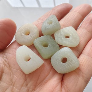 May include: Six white and green jade beads with holes in the center. The beads are various shapes and sizes.