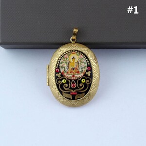 May include: Gold oval locket pendant with a black background and a colorful image of Buddha inside. The locket has a decorative border with red, yellow, and green accents.