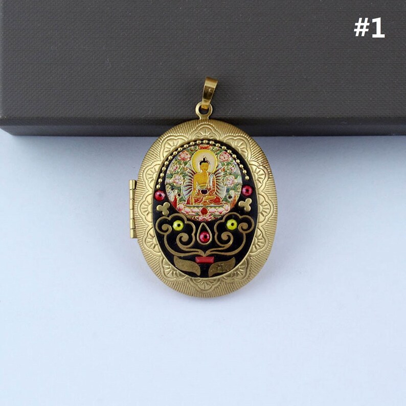 May include: Gold oval locket pendant with a black background and a colorful image of Buddha inside. The locket has a decorative border with red, yellow, and green accents.
