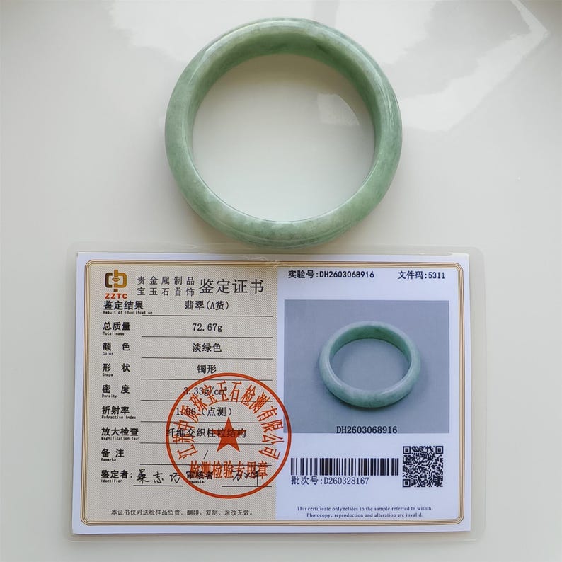 May include: A pale green jadeite bangle bracelet. The smooth, circular bracelet is displayed with a certificate that includes details such as the weight of 72.67 grams and the colour, which is described as pale green.