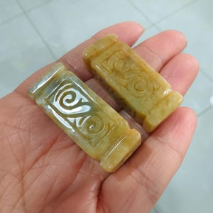Könnte beinhalten: Zwei gelb-grüne Jade-Anhänger mit aufwendig geschnitzten Designs. Die Anhänger sind rechteckig und haben eine glatte, polierte Oberfläche.