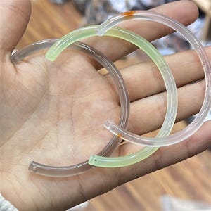 May include: Two jade bracelets, one green and one translucent white, with a slight orange hue. The bracelets are made of smooth, polished jade and are stacked on top of each other.