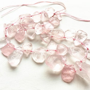 May include: A strand of pale pink rose quartz beads strung on pink thread. The beads are irregular in shape and have a translucent appearance.
