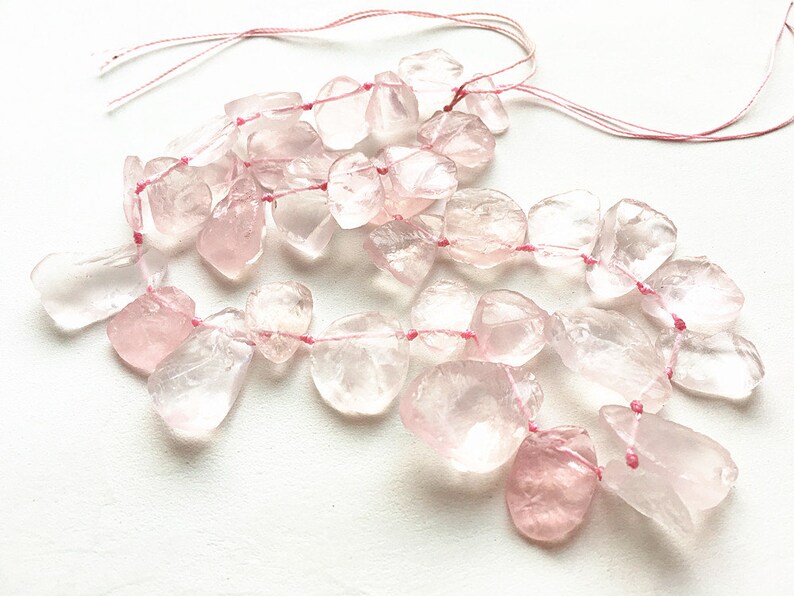 May include: A strand of pale pink rose quartz beads strung on pink thread. The beads are irregular in shape and have a translucent appearance.