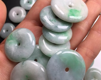 Puede incluir: Una colección de colgantes de jade verde y blanco en forma de rosquilla con un agujero en el centro. Los colgantes son lisos y pulidos.