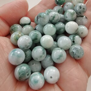 May include: A collection of round, green and white jade beads with a hole drilled through the center of each bead.