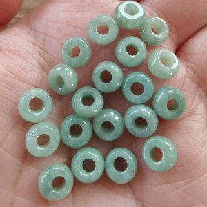 May include: A collection of 20 light green jade donut beads with a hole in the center. The beads are smooth and polished.