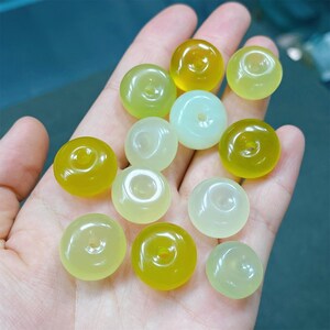 May include: A collection of 12 round, donut-shaped beads in shades of green and yellow. The beads have a hole in the center and are made of a smooth, polished material.