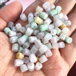 Pode incluir: Uma coleção de contas redondas e cilíndricas em tons de verde, branco e amarelo. As contas são feitas de jade e têm um acabamento liso e polido.