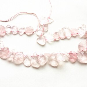 May include: A strand of pink rose quartz beads strung on pink thread. The beads are irregular in shape and have a translucent appearance.