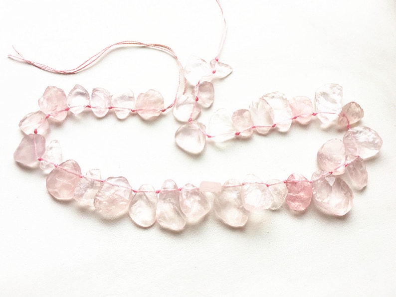 May include: A strand of pink rose quartz beads strung on pink thread. The beads are irregular in shape and have a translucent appearance.