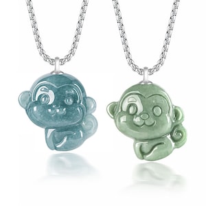 May include: Two silver necklaces with jade monkey pendants. The monkeys are carved in a cute, cartoon style and have green and blue jade coloring.