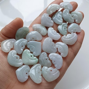 May include: A collection of heart-shaped jade pendants in various shades of green and white. Each pendant has a small hole for stringing. The pendants are smooth and polished, with a translucent appearance.