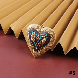 Puede incluir: Un medall&oacute;n de coraz&oacute;n de oro con un dise&ntilde;o detallado y una incrustaci&oacute;n de esmalte colorido con tres peces. El medall&oacute;n tiene un fondo marr&oacute;n oscuro con acentos azules, turquesa y rojos.