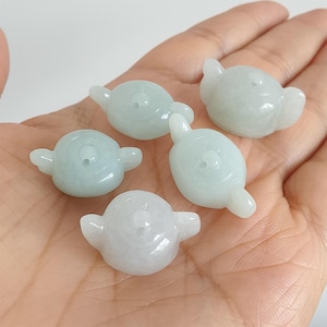 Könnte beinhalten: Fünf kleine, hellgrüne Jadeit-Steinschnitzereien in Form einer Teekanne. Jede Schnitzerei hat einen runden Körper, einen Ausguss und einen Henkel. Die Schnitzereien sind glatt und poliert, mit leicht durchscheinendem Aussehen.