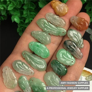 May include: A collection of jade leaf pendants in various shades of green, with a few orange and brown leaf pendants. The pendants are carved with intricate details and have a smooth, polished finish.