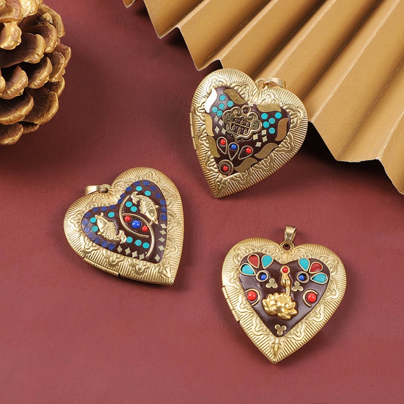 Puede incluir: Tres colgantes de coraz&oacute;n de oro con dise&ntilde;os intrincados. Cada colgante presenta un patr&oacute;n de esmalte colorido diferente con acentos turquesa, rojo y marr&oacute;n. Los colgantes est&aacute;n sobre un fondo rojo.