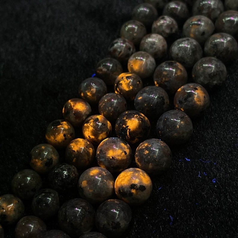 May include: A strand of black and orange gemstone beads. The beads are round and have a speckled pattern. The beads are arranged in a line, with the orange color showing through the black.