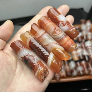 Puede incluir: Una colección de seis palitos de ágata con patrones de remolino de rojo, naranja y blanco. Los palitos son lisos y pulidos, y tienen un aspecto natural y orgánico.