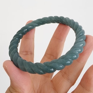Peut inclure: Un bracelet jonc en jade de couleur sarcelle avec un motif de corde torsadée. Le bracelet est lisse et poli, avec une légère translucidité. Le jonc est de forme circulaire, et le motif de corde entoure toute la circonférence.