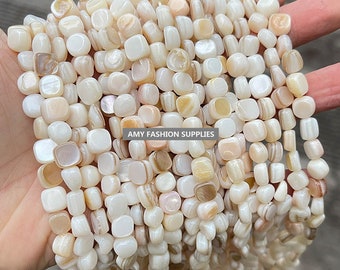 Puede incluir: Una hebra de cuentas cuadradas de color blanco y crema hechas de madreperla. Las cuentas tienen un brillo natural e iridiscente. Las cuentas están enhebradas en un hilo transparente y tienen aproximadamente 10 mm de tamaño. "AMY FASHION SUPPLIES" está impreso en una etiqueta blanca.