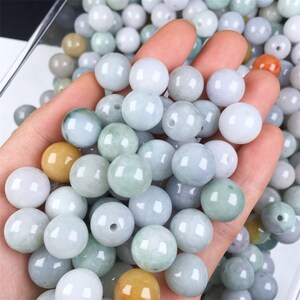 May include: A collection of round, smooth, jade green beads. The beads are various shades of green and some have a slight yellow tint.