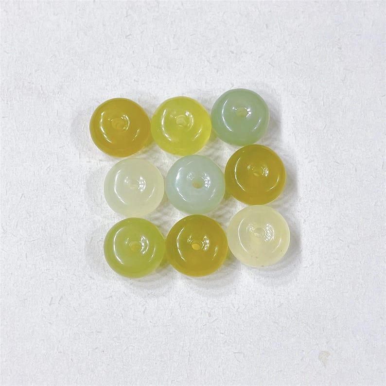 May include: Nine round jade beads in shades of green and yellow. The beads have a hole in the center and are strung together.