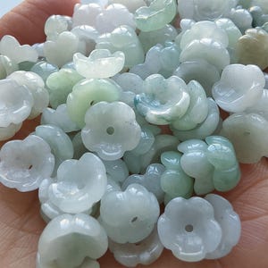 May include: A pile of translucent, flower-shaped beads in shades of white and green. Each bead has a central hole, and the petals are delicately carved. The beads are smooth and appear to be made of a polished stone.
