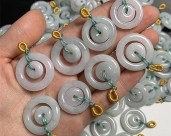May include: A collection of jade pendants with a double ring design. The pendants are strung on a green cord and have a gold loop at the top.