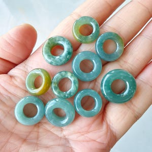 May include: Ten green jade stone rings with a hole in the center. The rings are various shades of green and have a mottled pattern.