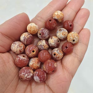 May include: A collection of round, red and white jasper beads with holes drilled through the center. The beads have a mottled, marbled appearance.