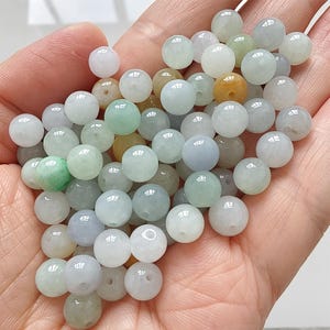 May include: A collection of round jade beads in a variety of colours, including white, green, and yellow. The beads are smooth and polished, with a slight translucence. These beads are suitable for jewellery making.