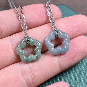 Puede incluir: Dos colgantes de jade con forma de flor en cadenas de plata. Los colgantes son ambos verdes, pero uno es de un tono de verde más claro que el otro.