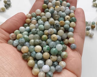 Puede incluir: Primer plano de una mano que sostiene numerosas cuentas redondas de varios colores, incluyendo verde, blanco y beige. Las cuentas parecen ser de piedra o un material similar. Las cuentas son pequeñas.