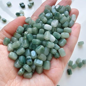 Puede incluir: Un puñado de cuentas de jade pulidas y pulidas en varios tonos de verde. Las cuentas son lisas y redondeadas, con un aspecto ligeramente translúcido. Adecuadas para la fabricación de joyas y proyectos de artesanía.