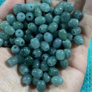May include: A collection of oval-shaped green jade beads. The beads are smooth and polished, with a light green colour.