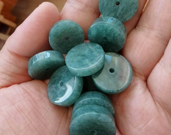 Può includere: Una collezione di dieci perle rotonde di giada verde con un foro al centro. Le perle sono lisce e lucidate.