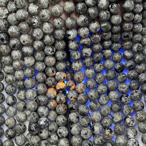 May include: A close-up of a strand of gray and black gemstone beads. The beads are round and have a speckled appearance.