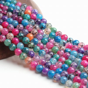 May include: A selection of colourful, round gemstone beads in shades of pink, blue, green, purple, and orange. The beads have a cracked, web-like pattern. The beads are strung together, for jewellery making.