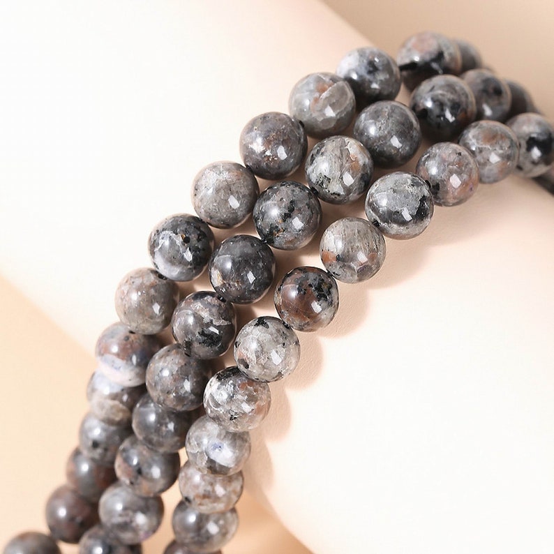 May include: A strand of black and grey gemstone beads. The beads are round and have a speckled appearance.