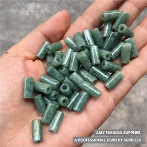 Puede incluir: Una colección de cuentas de jade verde, cada una con forma cilíndrica y un agujero perforado en el centro. Las cuentas son lisas y pulidas, con un brillo sutil.