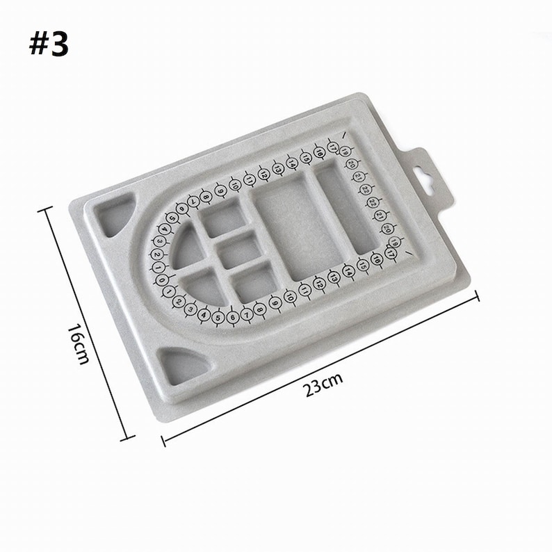 May include: Gray plastic jewelry making board with numbered circles around the edge and a grid of smaller squares in the center. The board measures 23 cm by 16 cm.
