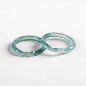 May include: Two jade green bangle bracelets with a smooth, polished finish. The bracelets are stacked on top of each other.
